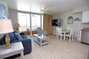 A living room with a sofa, a coffee table, a TV, and a dining area with chairs and a table. - Casa Playa Beach Resort (Fort Myers Beach)