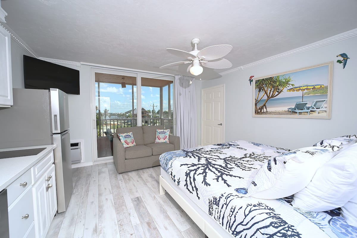 Une chambre à coucher avec un lit, un ventilateur de plafond, une fenêtre donnant sur un beau paysage, une porte et un tableau accroché au mur.