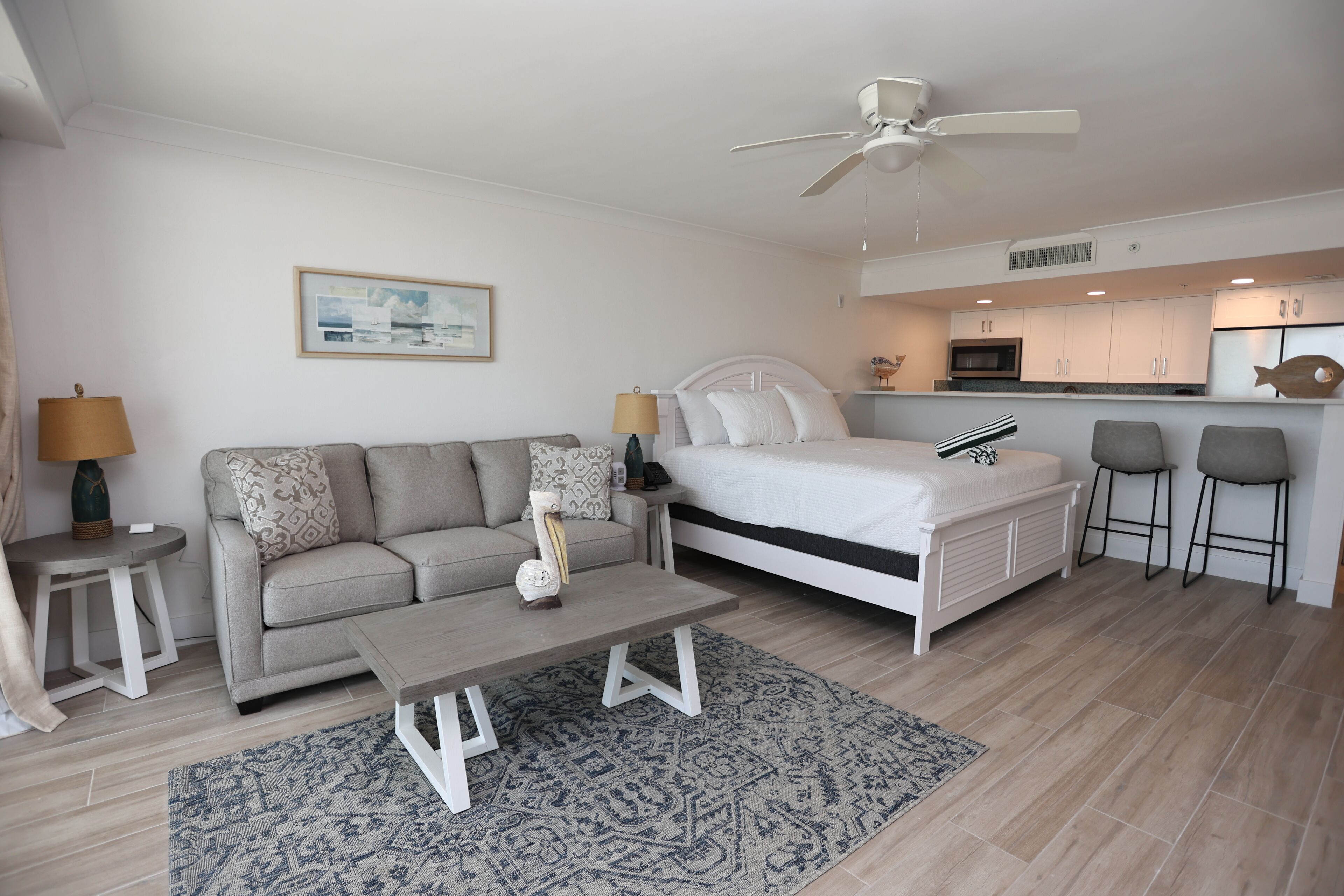 A modern, well-lit room with a sofa, a bed, a coffee table, and a kitchen area with a refrigerator and microwave.