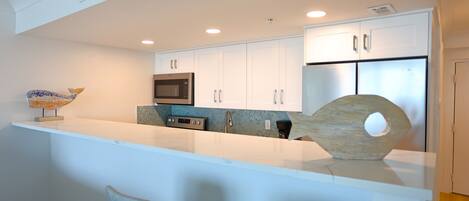 A modern kitchen with white cabinetry, a built-in microwave, and a stainless steel refrigerator.