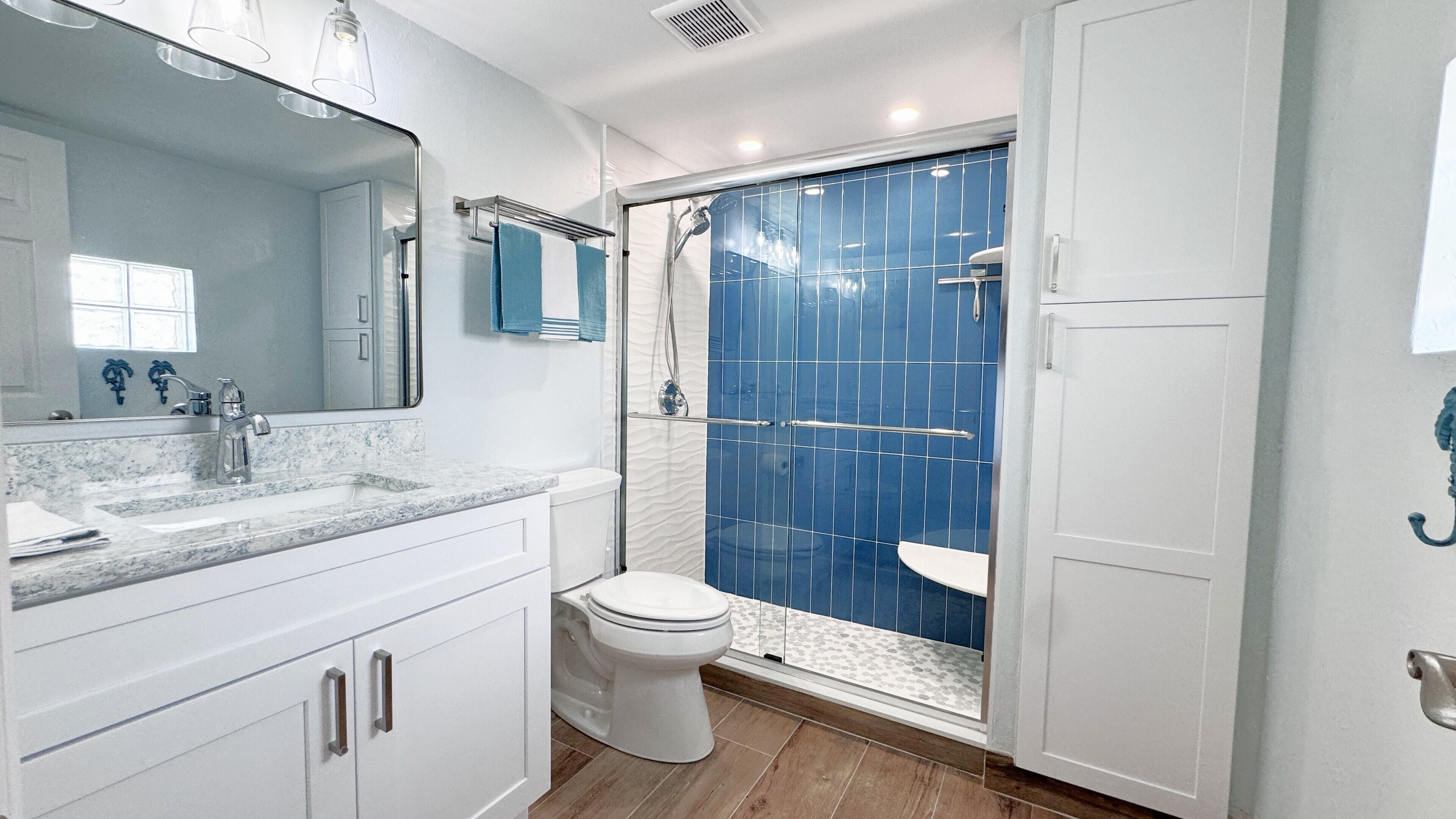A modern bathroom with a marble sink, a toilet, and a glass-enclosed shower.
