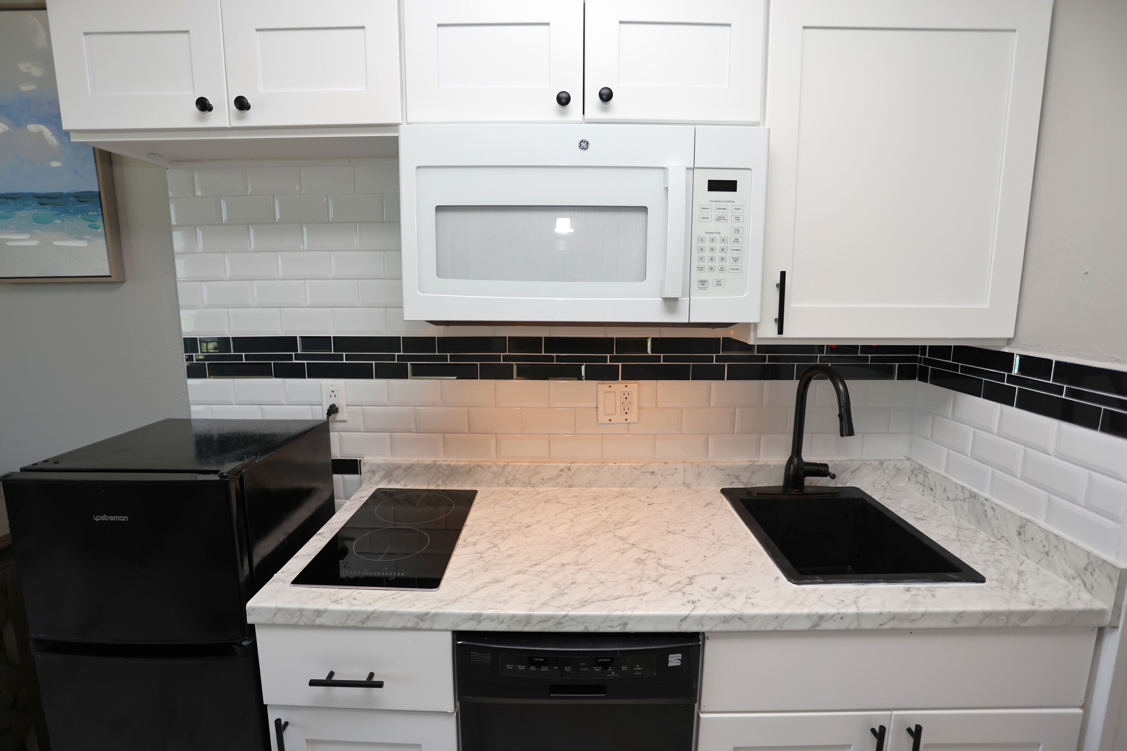 A kitchen with white cabinets, a microwave, a black induction cooktop, a dishwasher, and a black refrigerator.