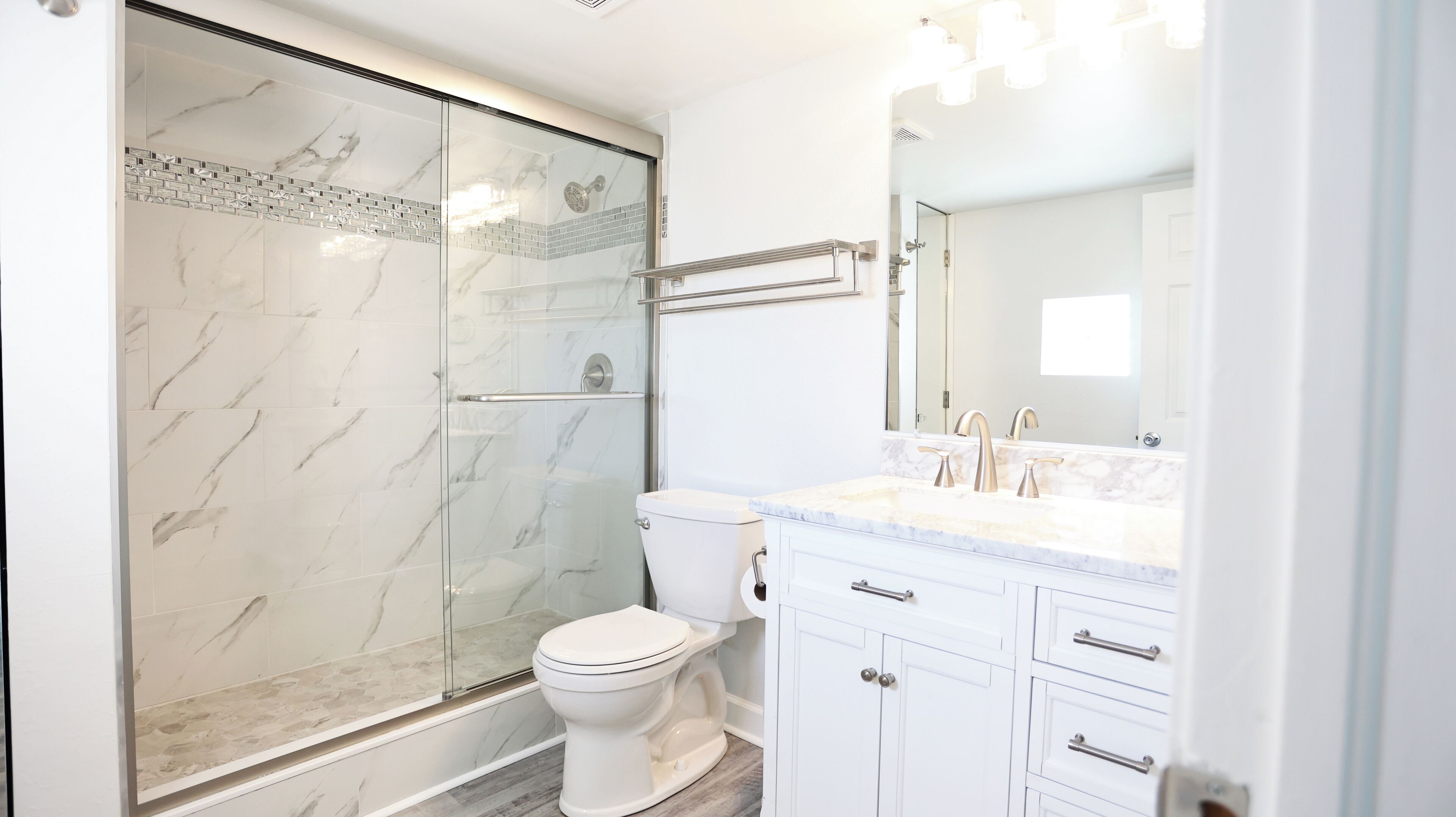 A modern bathroom with a glass shower enclosure, a toilet, a sink with a mirror, and white cabinetry.