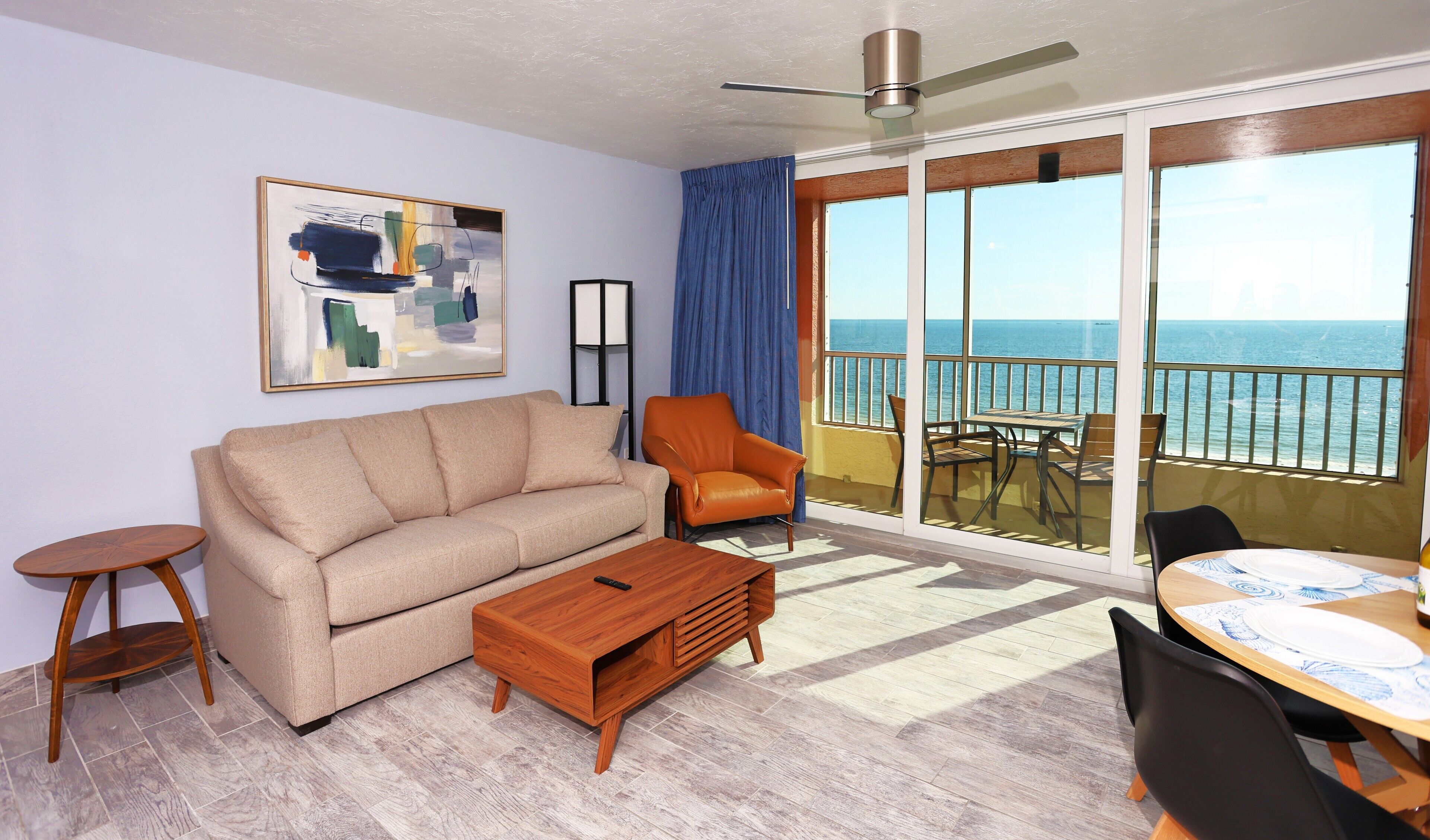 A living room with a sofa, armchair, coffee table, and a balcony with a table and chairs.