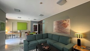 A modern living room with a green sectional sofa, a black coffee table, and a painting on the wall.