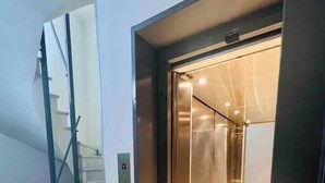 A modern elevator with a glass door, a marble staircase, and a metal handrail.