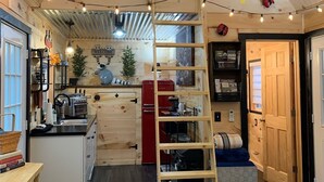 A cozy kitchen with wooden walls, a central island, and a ladder leading to a loft area. - Raccoon Lodge at Coops Creek Cabins (Dunlap)