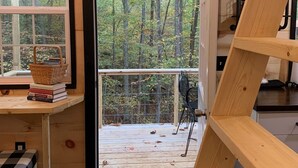 A wooden cabin interior with a wooden staircase, a window with a view of a forest, and a door leading outside. - Raccoon Lodge at Coops Creek Cabins (Dunlap)
