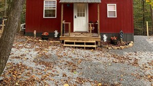 A red cabin with a metal roof, a front porch, and a gravel driveway surrounded by trees. - Raccoon Lodge at Coops Creek Cabins (Dunlap)