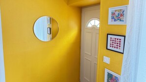 Un corridoio con pareti gialle, una porta bianca, uno specchio e quadri appesi.