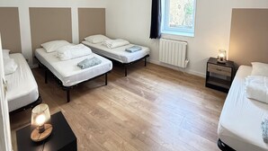 Una stanza con tre letti, una finestra con tende, un termosifone e un comodino con una lampada.