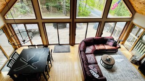 A spacious room with a large window, a leather sofa, a dining table, and a small round table. - Modern Chalet Near Mt. Sunapee & Lake Massasecum (Bradford)