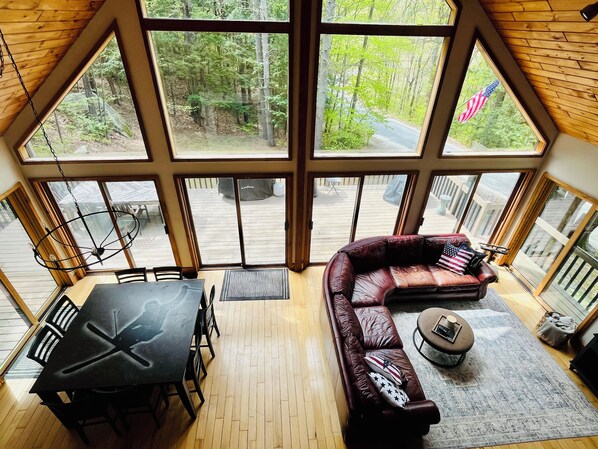A spacious room with a large window, a leather sofa, a dining table, and a small round table.