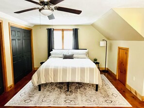A bedroom with a bed, a ceiling fan, a window with curtains, a nightstand, and a floor lamp.