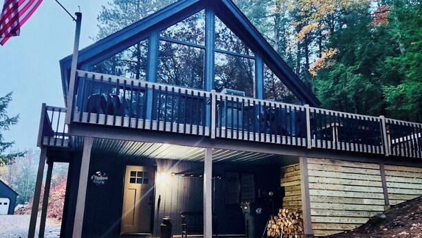 A cabin with a balcony, a flag, and a forested background. - Modern Chalet Near Mt. Sunapee & Lake Massasecum (Bradford)
