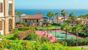 Ett semesterhotell med en tennisbana, palmer och utsikt över havet.