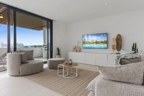 A modern living room with a curved sofa, a round coffee table, and a flat-screen TV mounted on the wall. - Viva la Vida | sea views - pool - terrace (Fuengirola)