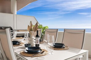 A dining table set for two with a view of the ocean, a bottle of wine, and a vase with dried leaves. - Viva la Vida | sea views - pool - terrace (Fuengirola)