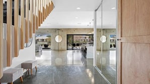 A modern interior with a long corridor, seating area, and a glass wall offering a view of the outdoors. - Luxico Urban Hideaway (Pet Friendly) (Broadbeach Waters)