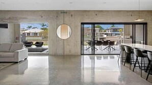 A spacious living area with a large window, a round mirror, a sofa, and a dining area with chairs and a table. - Luxico Urban Hideaway (Pet Friendly) (Broadbeach Waters)