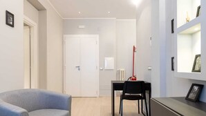 Una habitación moderna con un sofá gris, una mesa de comedor con una silla negra, un extintor rojo y un cuadro en un mueble.