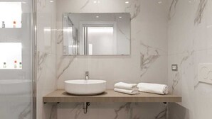 Un baño moderno con pared de mármol, un lavabo redondo, un inodoro y un box de ducha de vidrio.