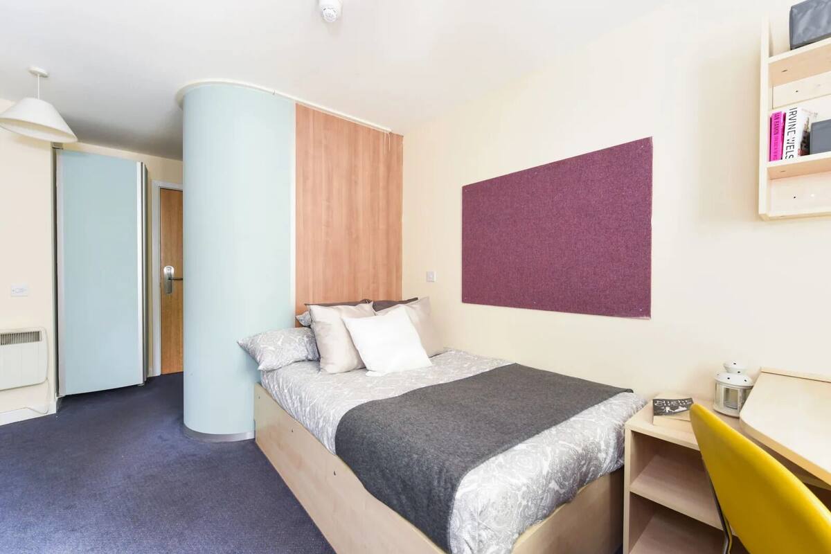 A bedroom with a bed, a desk, a chair, a bookshelf, and a door.