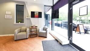 A modern interior with two grey armchairs, a small table, and a large window offering a view of parked cars outside. - Student Only Gibson Street (Glasgow)