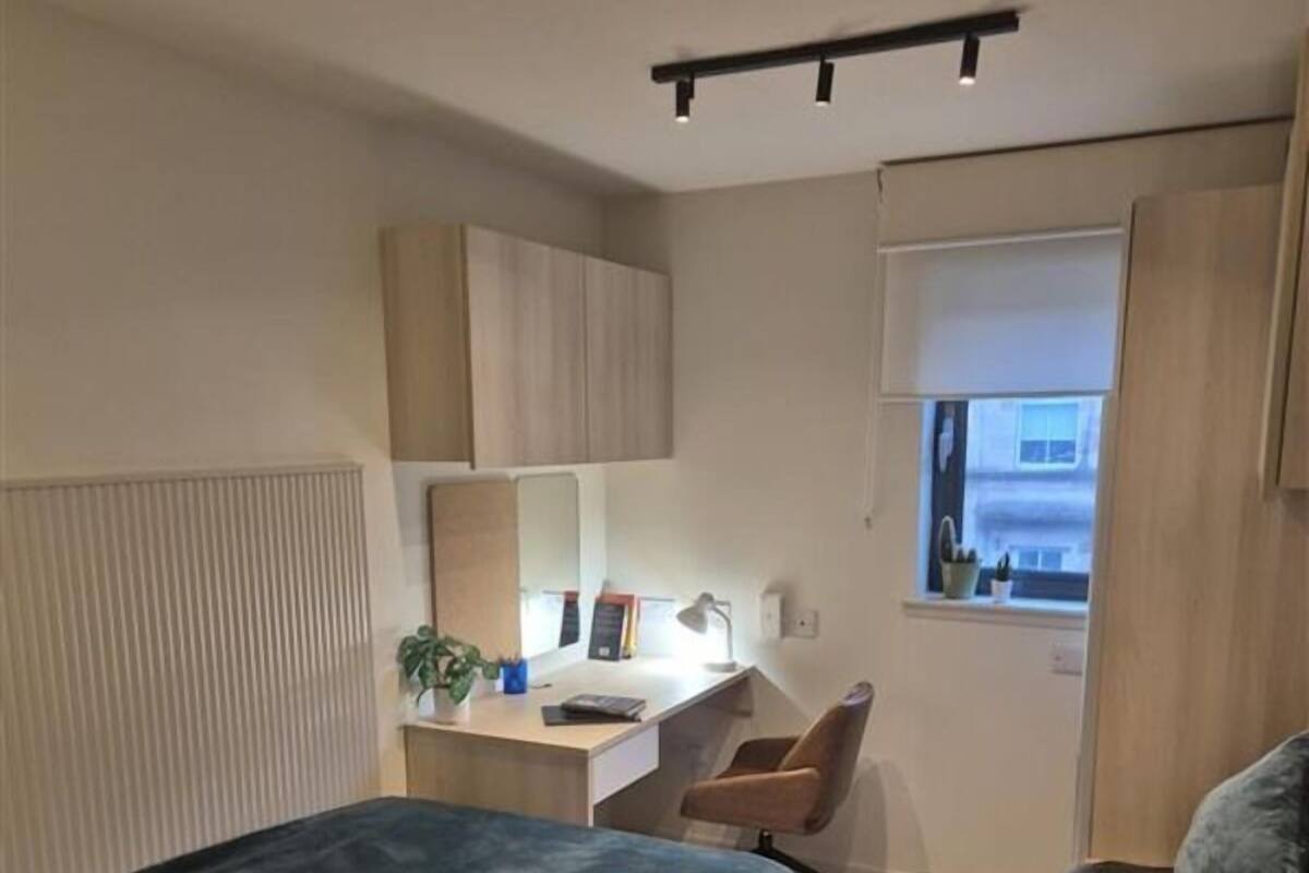 A modern bedroom with a bed, a desk, a chair, and a window.