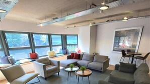 A modern lounge area with sofas, chairs, and a coffee table. Large windows provide natural light and a view of the outdoors. - Student Only Gibson Street (Glasgow)