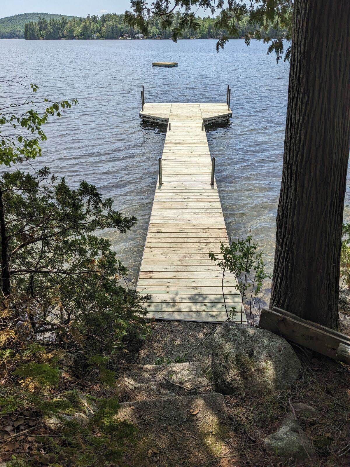 A wooden dock extending into a calm lake, surrounded by trees and rocky terrain.