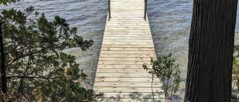 A wooden dock extending into a calm lake, surrounded by trees and rocky terrain.