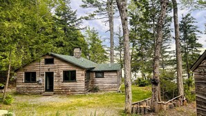 A rustic log cabin with a chimney, surrounded by tall trees and a grassy yard. - Welcoming 4-bedroom lake front cabin in charming Otis on Beech Hill Pond. (Otis)