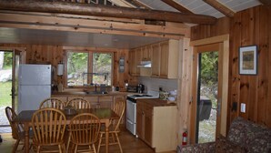 A cabin interior with a dining area, kitchen, and a view of the outdoors. - Welcoming 4-bedroom lake front cabin in charming Otis on Beech Hill Pond. (Otis)