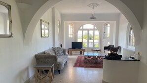 A spacious living area with a sofa, a coffee table, and a TV. There are arched windows and a view of the outdoors. - Large house with private swimming pool, enclosed grounds that will enchant your vacations.  (Saint-Ambroix)