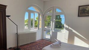 A bedroom with a bed, a radiator, a standing lamp, a patterned rug, and large arched windows. - Large house with private swimming pool, enclosed grounds that will enchant your vacations.  (Saint-Ambroix)