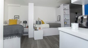 A modern bedroom with a bed, bedside tables, a nightstand, a wardrobe, and a kitchenette area. - Student Only The Cube Ealing (London)