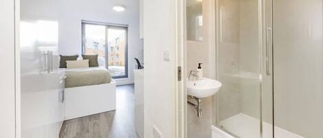 Un baño moderno con cabina de ducha de vidrio, un lavabo blanco y una mesita de noche con lámpara.