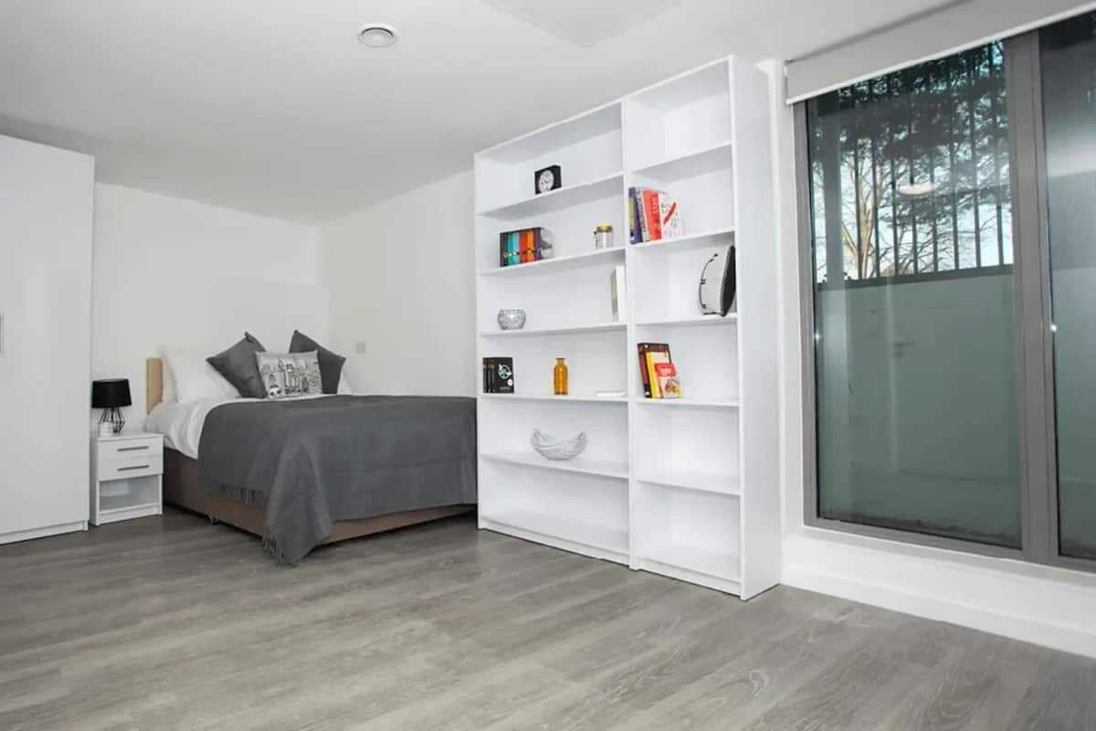 Un dormitorio moderno con cama, armario blanco, estantería empotrada y puerta corredera de cristal al exterior.