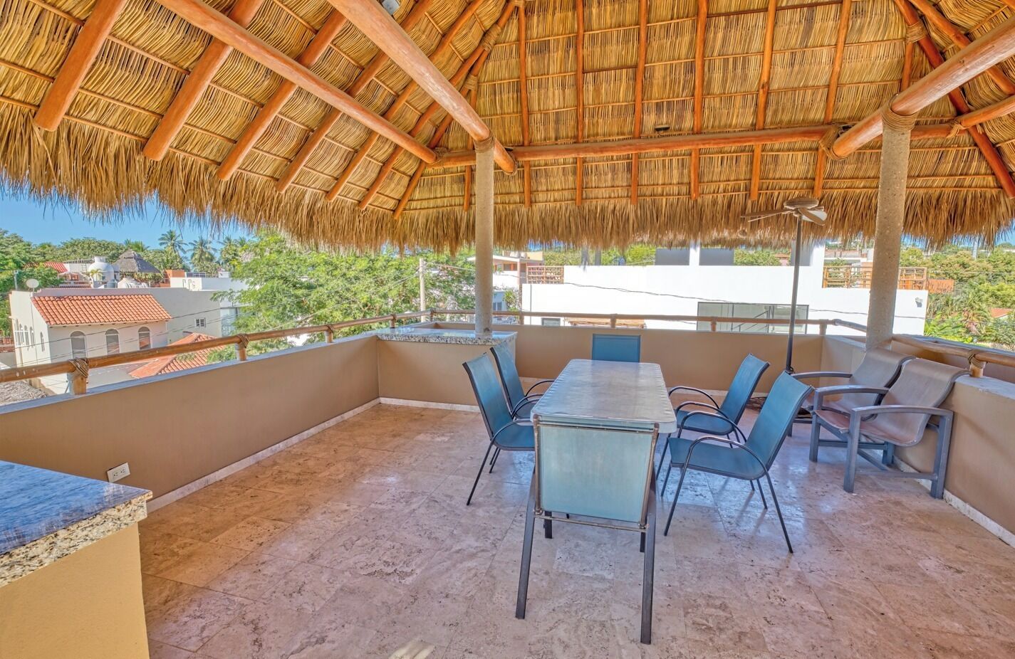 A covered outdoor seating area with a thatched roof, a table, and chairs.