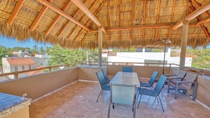 A covered outdoor seating area with a thatched roof, a table, and chairs. - Casa Piedra: 4BR/4BA, Private Pool & Rooftop Palapa, Sleeps 8 San Pancho Nayarit (San Francisco)