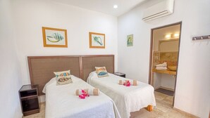 A hotel room with two beds, a small bedside table, an air conditioning unit, and a bathroom with a mirror and sink. - Casa Piedra: 4BR/4BA, Private Pool & Rooftop Palapa, Sleeps 8 San Pancho Nayarit (San Francisco)