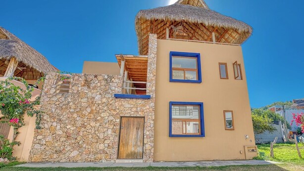 A two-story building with a stone facade, a wooden door, and a thatched roof. - Casa Piedra: 4BR/4BA, Private Pool & Rooftop Palapa, Sleeps 8 San Pancho Nayarit (San Francisco)