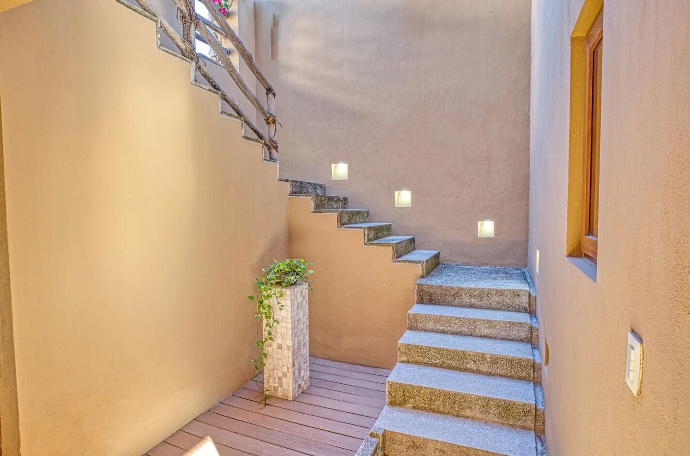 A narrow staircase with stone steps and wall-mounted lights, leading to a wooden deck area.