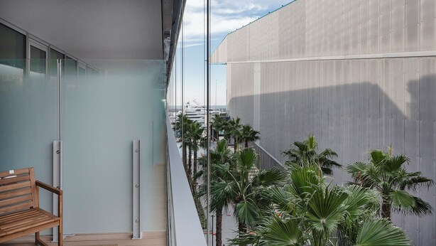 A balcony with a wooden bench, a glass railing, and a view of a marina with boats and palm trees. - Waterfront Vibes by Wonderful Italy (Genoa)