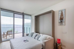 A modern hotel room with a large bed, a small sofa, a painting of a sailboat, and a view of the balcony. - Waterfront Vibes by Wonderful Italy (Genoa)