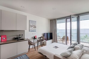 A modern hotel room with a bed, a desk with a chair, a TV, and a balcony with a table and chairs. - Waterfront Vibes by Wonderful Italy (Genoa)