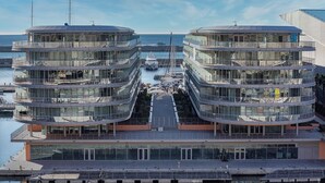 A modern multi-story building with a glass facade, located near a marina with boats. - Waterfront Vibes by Wonderful Italy (Genoa)