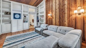 A modern living room with a sectional sofa, built-in shelving, and a wooden accent wall. - Luxury Austin Estate – Tranquil, Spacious & Packed with Games and Pool. (Austin)