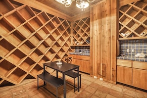 Interior de madera con una mesa y banco, zona de cocina con azulejos azules y techo de madera con diseño en forma de cruz.